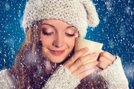 Beautiful woman in warm sweater with snowflakes around her, on blue background